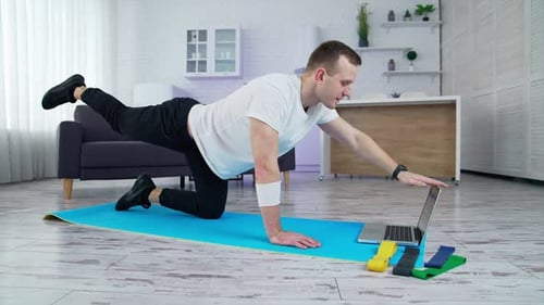 Young lifestyle sportsman working out in front of his laptop computer at home.