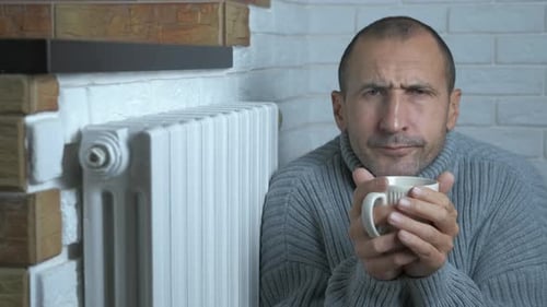A Man Freezes at Home Near the Heating Radiator