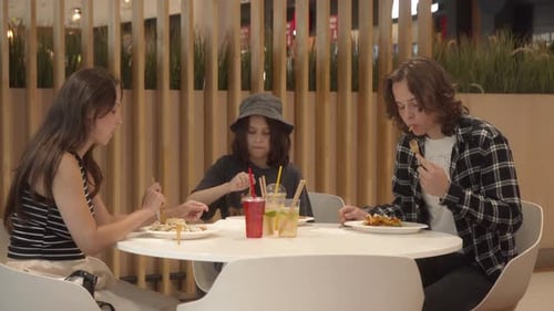 A woman with her kids is having lunch at a table in a mall food court.