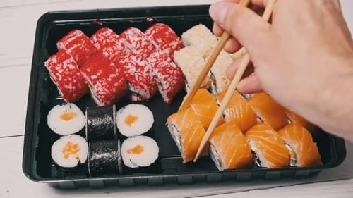 Sticks Take Sushi From the Plastic Sushi Box CloseUp