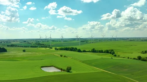 Luftaufnahme eines Windparks in einer ländlichen Gegend mit Windturbinen, die über grüne Felder unter einem