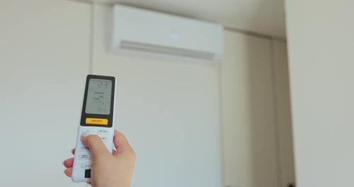 Adjusting Air Conditioner with Remote Indoors on White Wall