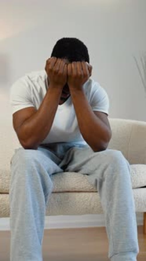 Man Sitting on Couch Holding Head