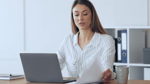 Young Woman Working on a Laptop at a Desk in a Bright Office Space