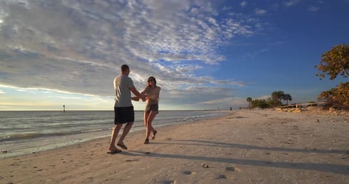 Romantic couple walking holding hands on a beautiful beach at sunset together
