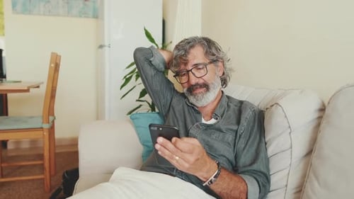 Adult Man Relaxing Using Smartphone on Couch at Home