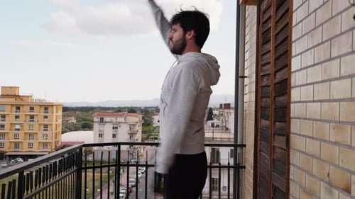 Man Stretching Arms on Balcony in City