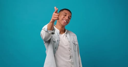 Young African American Man Pointing Index Finger on Camera Standing Over Blue Studio Background