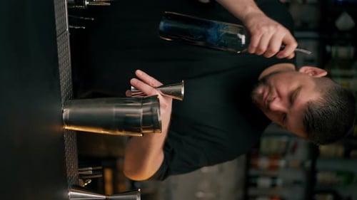 Vertical Video Closeup a Male Bartender Hands Holding Bottle and Masterfully Pours Liquor Into Steel