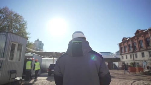 Worker in Helmet Walks Construction Site Under Sunny Sky