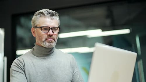 Close up of concentrated mature gray-haired bearded businessman in glasses typing on laptop at work