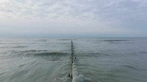 Aerial establishing view of an old wooden pier at the Baltic sea coastline, overcast winter day, whi