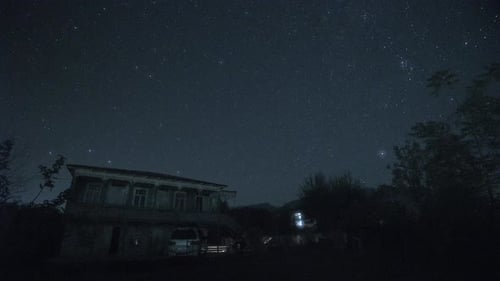 Landscape of Night Sky with Shining and Rotating Stars Over Mountain Village in Timelapse