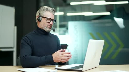Man Communicates on Laptop in Office with Headset