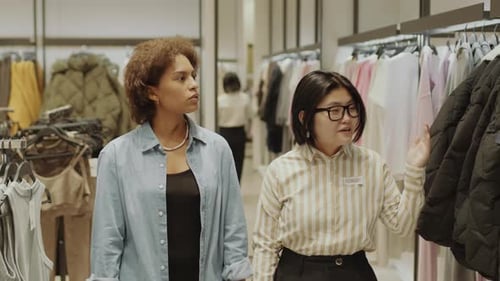 Asian Shop Assistant Showing Customer around Clothing Store