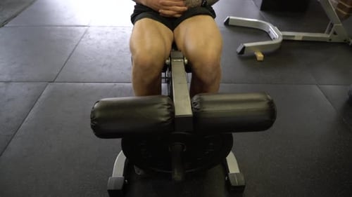 Homem tatuado em máquina de extensão quádrupla de ginástica doméstica