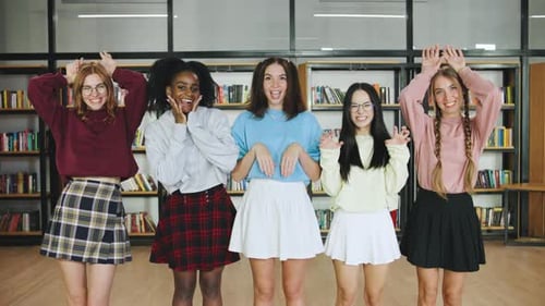 Cinco jovens estudantes multirraciais posam de brincadeira e fingem ser quadriláteros na biblioteca