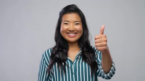 Smiling woman gives thumbs up on gray background