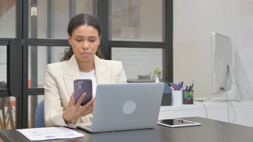 Woman Working with Phone and Laptop in Office