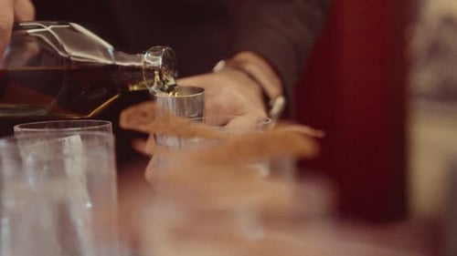 Serveur versant du whisky provenant d'un doseur en métal dans de petits verres