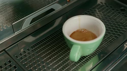 Pouring coffee flows from the machine into the cup making hot drink using the filter holder
