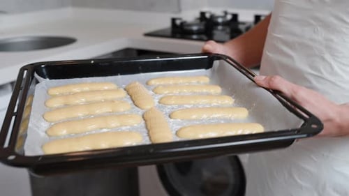 The choux pastry for eclairs is placed on a baking sheet, and the woman puts it into the oven.