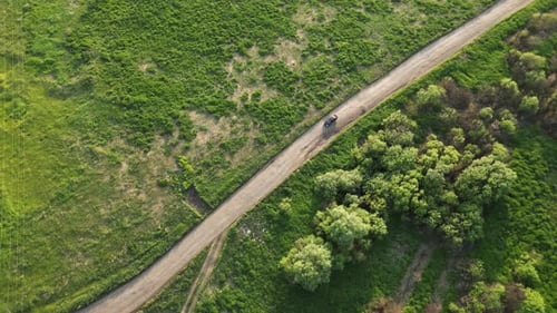 Black Car Driving Narrow Dirt Road Across Green Pasture Revealing Rural Landscape From Elevated