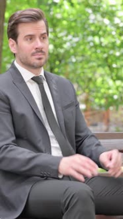 Man in Suit Sits on Bench Checking Time