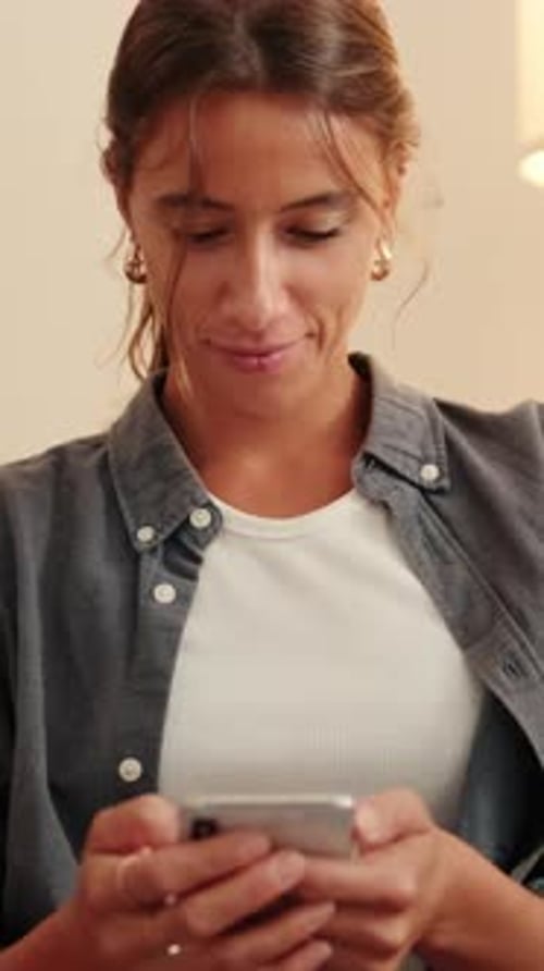 Smiling Woman Uses Smartphone Indoors
