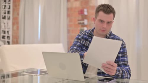 Young Adult Reacts Negatively to Paperwork at Desk