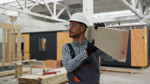 Construction Worker Carrying Lumber in a Building Factory