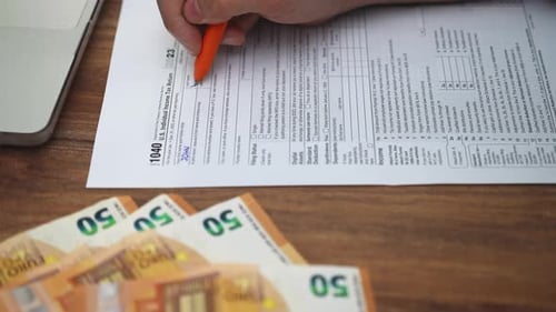 Un jeune entrepreneur écrit méticuleusement sur un formulaire papier 1040 détaillant les revenus de démarrage