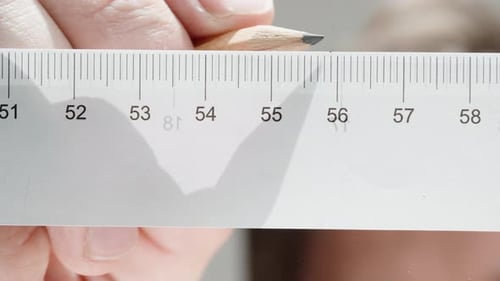 Taking measurements, close-up on a man making pencil marks. Ruler with centimeter scale. Low angle.