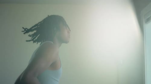 Junger Mann mit Dreads trainiert zu Hause mit Sonnenlicht auf einem Laufband