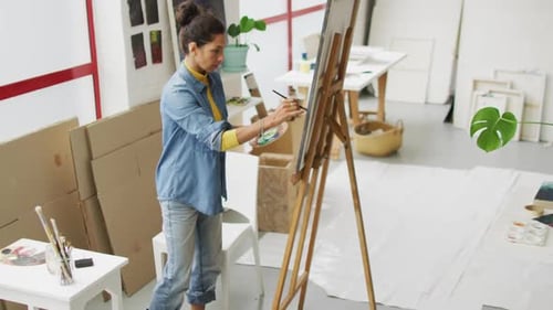 Video of biracial female artist painting in studio