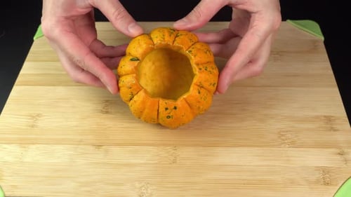 Hands placing fresh decorative pumpkin on a cutting board for preparing a Halloween dish. Festive