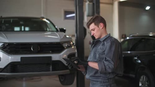Junger professioneller männlicher Autoservice-Mitarbeiter mit Tablet in der Hand reguliert Rise of Car am