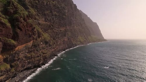 Drone footage of a mountain by the sea in stunning capturing dramatic cliffs, blue ocean, and