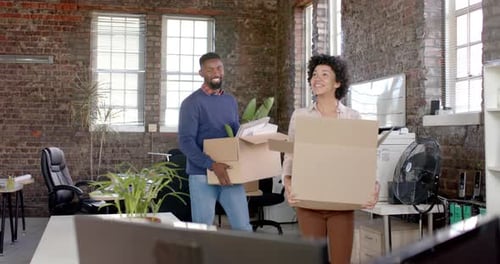 Happy diverse colleagues holding boxes with documents and office items in slow motion