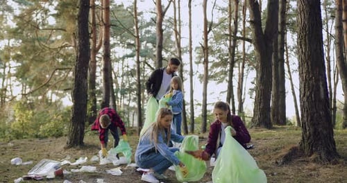 Woman's volunteers picking up rubbish into the plastic bags from park territory and giving high five