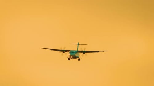 Turboprop Aircraft Flying with Propellers Spinning and Landing Gear Down Against Orange Sunset Sky