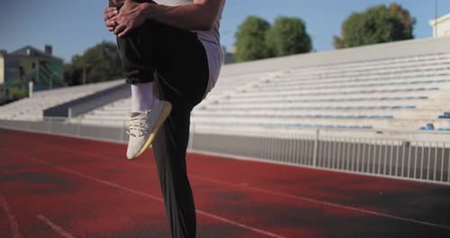Young African American Man in Sportswear Stretches His Joints at the Stadium
