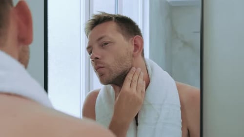 Man Examines His Face in Bathroom Mirror