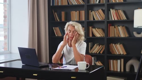 Woman Working at Desk Removing Glasses and Rubbing Eyes