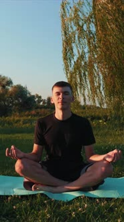 Man practicing yoga exercises on fitness mat at park in morning. Vertical video