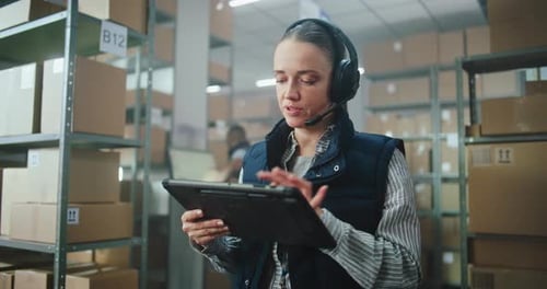 Woman uses tablet with headset in warehouse