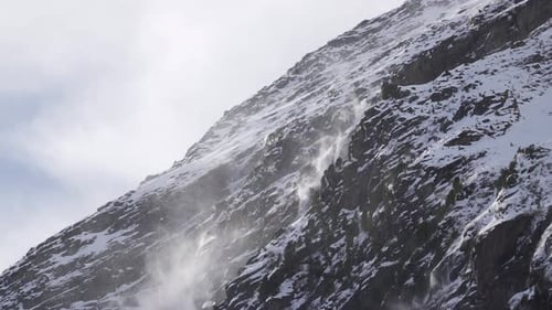 Nahaufnahme von Schnee, der von einem Bergkamm an einem schneebedeckten felsigen Gletscherhang geblasen wird