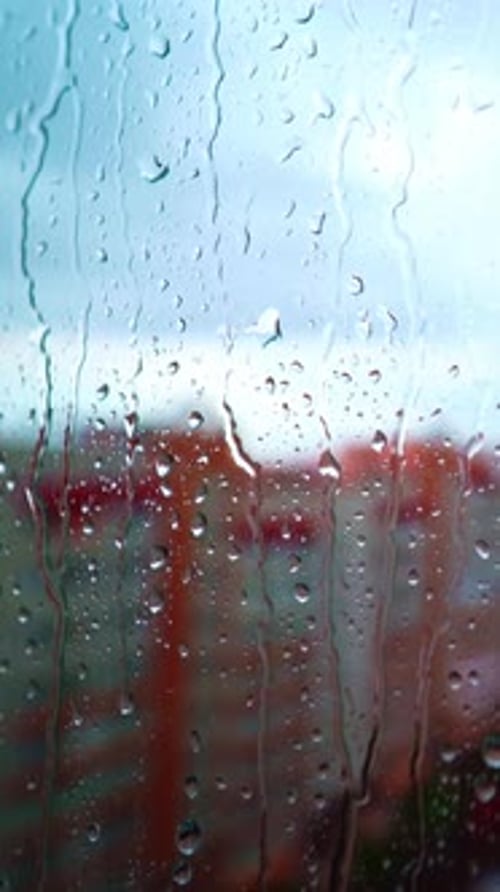 Raindrops on window in the city. Rainy weather with a sun on the sky.