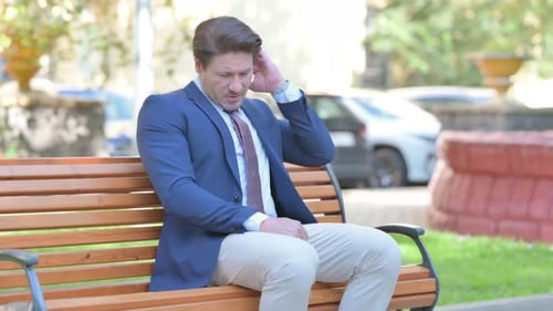 Man Suffering Headache Sitting on a Park Bench