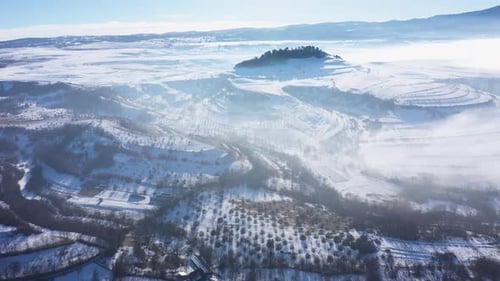 Aerial view of misty countryside hills at wintertime, morning fog above by drone